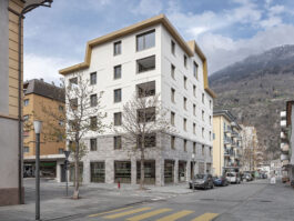 Klassisches Gebäude mit klaren Linien und einem goldenen Dach, eingebettet in die Stadtlandschaft von Brig im Oberwallis – ein Beispiel zeitgenössischer Architektur von Architekten der Region Oberwallis.