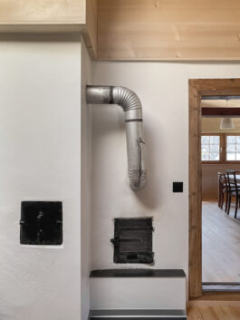 Detailfoto des alten Kamins im Umbau eines Walliserhauses in Lax, Goms: Nahaufnahme des historischen Kamins, kombiniert mit modernem Design, Blick in den Wohn- und Essbereich, entworfen von Architektur Holzer GmbH.